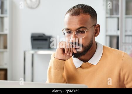 Pensive young middle eastern man in eyeglasses leaning head on hand while working with analytics in office Stock Photo