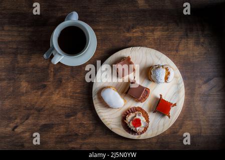 Small cakes on a rustic wooden plate, next to coffee on an old wooden table. Stock Photo