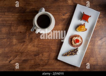 Small cakes on a white plate, next to coffee on an old wooden table. Stock Photo