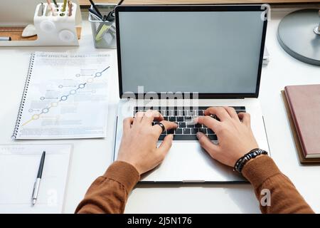 Above view of unrecognizable manager sitting at desk with document and preparing strategy plan on laptop Stock Photo