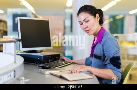 Asian student girl is working with a book while sitting in front of a computer Stock Photo