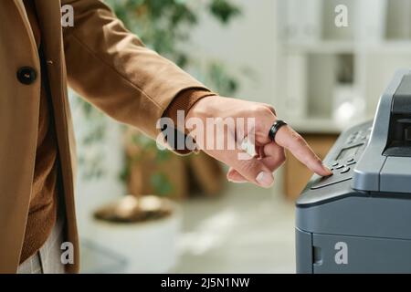 Close-up of male hand in ring pushing button on scanner while working with documents in office Stock Photo