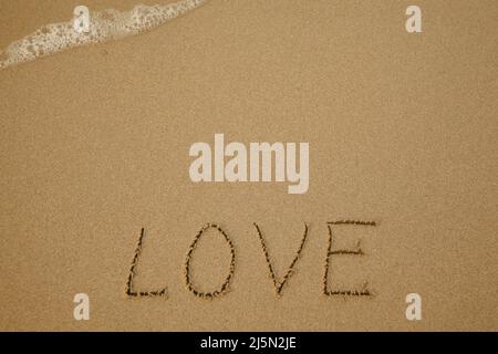 Love - handwritten on the soft beach sand. Stock Photo