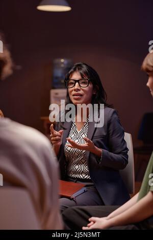 Vertical shot of modern psychotherapist working with group of people having depression discussing something with them Stock Photo