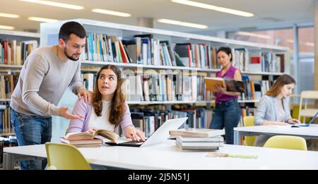 Male librarian helping focused adult student preparing to exam Stock Photo