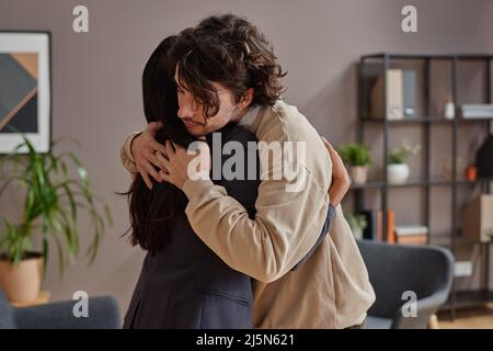 Horizontal medium shot of young man suffering depression getting support from professional psychologist hugging her Stock Photo