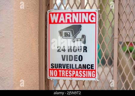 Surveillance camera signage on a metal mesh wire railings at San Francisco, California. 24 hour video surveillance no tresspassing sign against the li Stock Photo