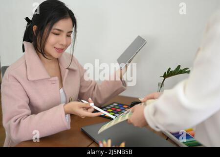 Successful millennial Asian female graphic designer manager working with her assistant at her desk. Stock Photo