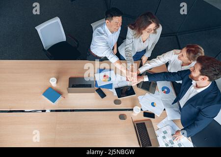 Diverse business people group put hands together while standing near the table in office Stock Photo