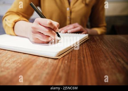 hand of an unrecognizable caucasian young woman writing with a pen on a paper notebook Stock Photo