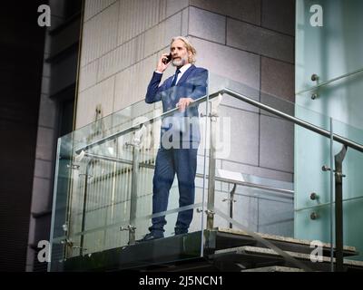 mature caucasian corporate business man standing on top of stairs making a call using cellphone in modern office building Stock Photo