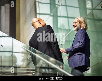 caucasian and latino corporate business men talking chatting having a conversation while walking on stairs in modern office building Stock Photo