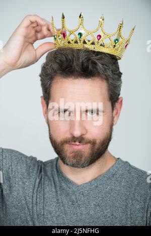 Young man with golden crown of king over gray background. Handsome man wearing king crown. Stock Photo
