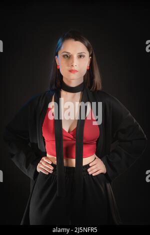 Studio shot of a woman in her 30s wearing black pajamas and a red short tank top. Stock Photo