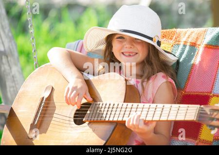 Musician child playing guitar. Kid girl singing and playing guitar outside. Kids music and songs. Smiling child playing outdoors in summer. Stock Photo