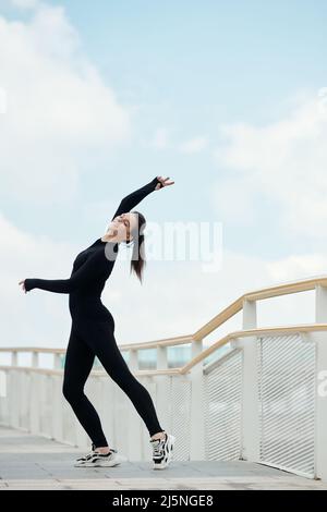 Happy slim fit female ballet dancer enjoying dancing on bridge Stock Photo