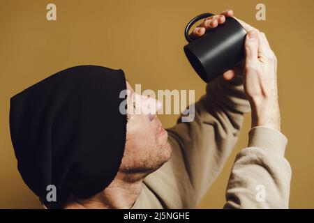 A man with surprise looks into a black cup. Portrait of a young man in a black cap Stock Photo