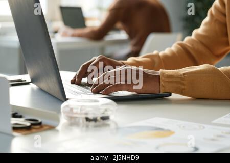 Close-up of unrecognizable office man in sweater sitting at table and typing on laptop Stock Photo