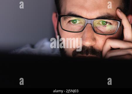 Close up of young adult man in glasses working on laptop computer at night Stock Photo