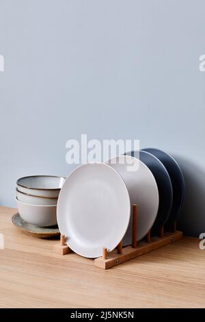Set of modern ceramics plates on a stand with stack of bowls behind them on table Stock Photo