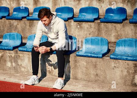 Man in sportswear resting at stadium seat and use smartphone Stock Photo