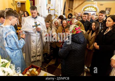 Ukrainian faithful receive blessing from the priest during the Easter Sunday service, called Holy Pascha at Greek-Catholic church. Holy Pascha in Ukraine took place on Sunday morning instead of traditional midnight due to military curfew. As the Russian Federation invaded Ukraine nearly two months ago, the conflict forced more than 10 million Ukrainians to flee the war zones, both internally and externally. Nadyby village and its Greek Catholic church became a shelter for dozens of refugees from Kharkiv, Donesk and Zaporizhzhia Oblast. As Ukrainian faithful gather for orthodox Easter celebrati Stock Photo