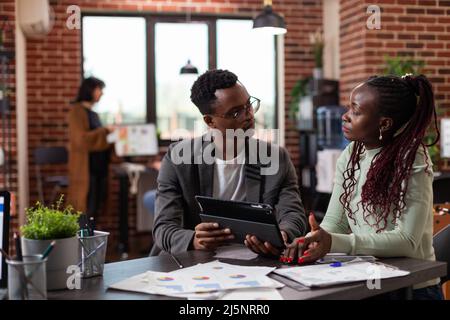 Executive managers analyzing marketing statistics using tablet computer working at company project during business meeting in startup office. Diverse team brainstorming ideas planning strategy Stock Photo