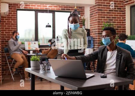 Executive managers working at marketing project analyzing company statistics planning business collaboration in startup office. Multiethnic businesspeople with medical face mask against covid19 Stock Photo