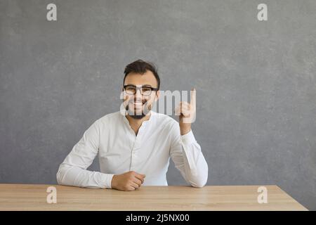 Attractive young man in white shirt pointing with finger up against gray background Stock Photo