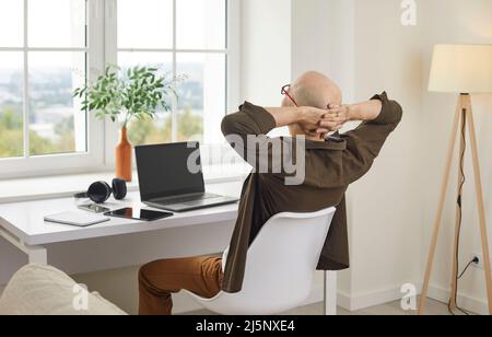Businessman taking break and relaxing while working on laptop in his home office Stock Photo