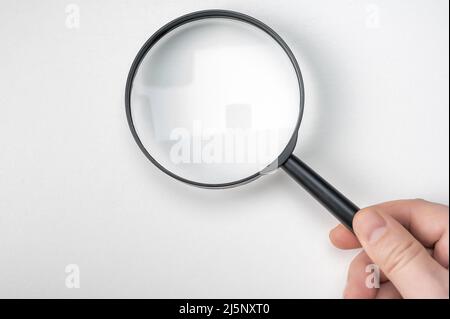 Hand holding magnifying glass isolated on white background. man hand holding black magnifying glass. Research, searching or investigating something. t Stock Photo