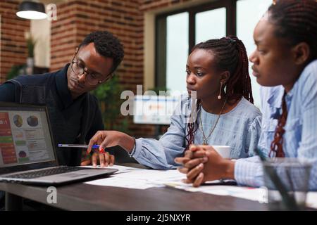 Research agency employee pointing out financial data error on laptop screen. African american business people discussing about startup project method of development and future expenses. Stock Photo