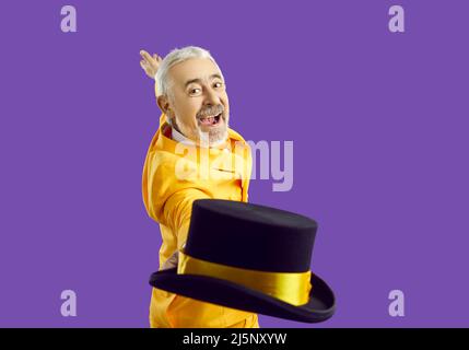 Happy excited senior man in yellow suit smiles, takes off his top hat and looks at camera Stock Photo