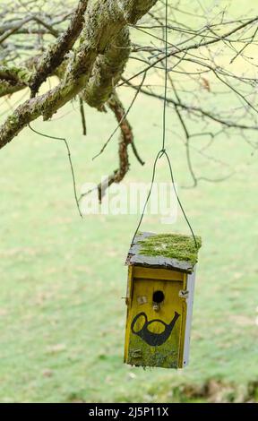 Wooden bird nesting box hanging on a wire from a tree with painted sign for post or mail Stock Photo