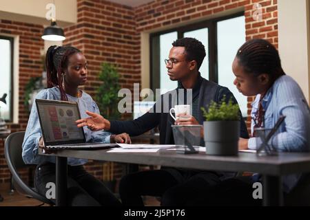 Financial company african american accountant pointing out on laptop wrongly declared revenues. Marketing department team members discussing about imminent business bankruptcy. Stock Photo
