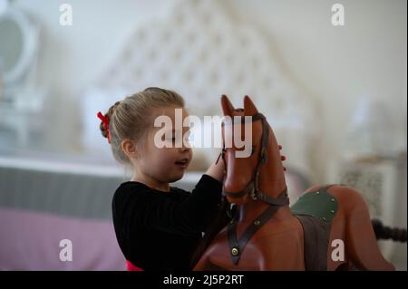 beautiful little girl with a toy wooden horse in a vintage studio. Stock Photo