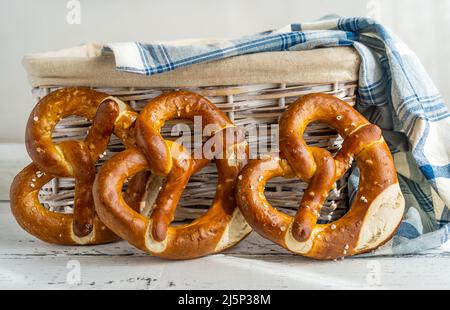 Three brezels or pretzels placed near bread basket with napkin on white wooden background Stock Photo