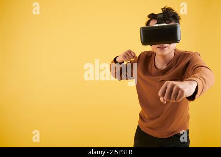 Young man wearing virtual reality headset when fighting with enemy in video game Stock Photo