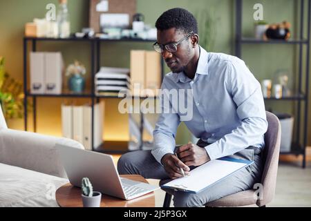 Young Black psychiatrist in glasses talking to client in online therapy session and talking notes Stock Photo