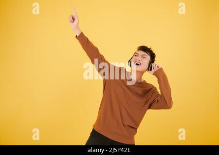 Excited young man dancing to the music in headphones, isolated on yellow Stock Photo