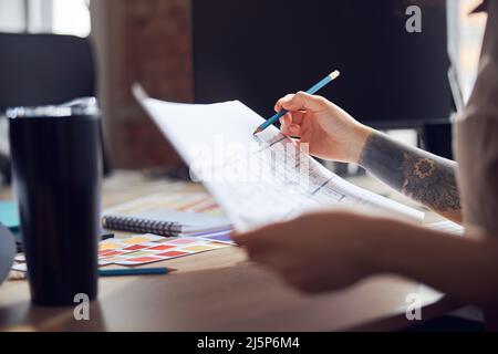 Close up shot of female interior designer working on a project with bluepint, making notes, sitting at the desk in her office Stock Photo