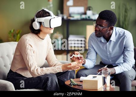 Software developer giving plastic spider to young woman wearing virtual reality headset Stock Photo