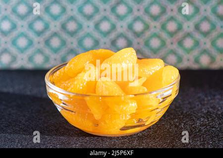 Small glass bowl filled with mandarin oranges compote, large peeled slices of fruit in juice, delicious dessert and healthy snack served on its own Stock Photo