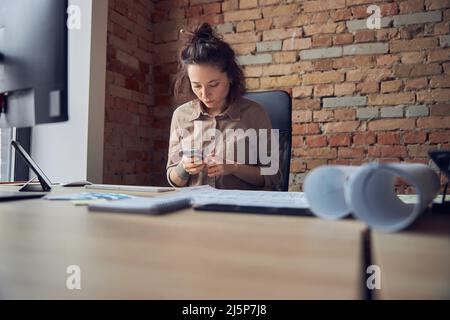 Female interior designer using smartphone while working in her office Stock Photo