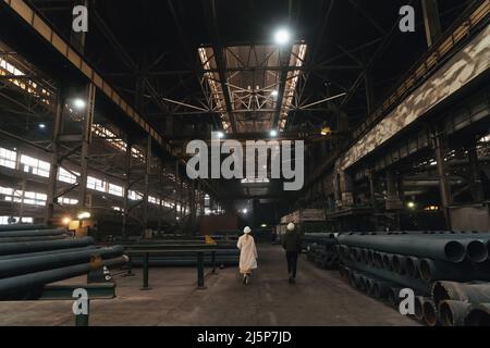 Two female workers in hard hats side view in large factory warehouse interior. Stock Photo