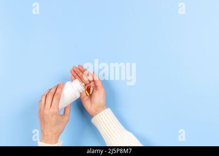 Colorful medicine pills and capsules in woman hand on pastel blue background. Female hand spilling pills out of white bottle. Pharmacy, medicine and Stock Photo