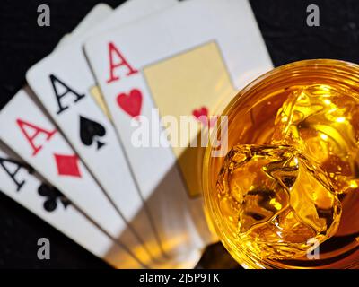 Glass of whiskey with ice cubes on poker playing cards with four aces. Poker game gambling and whisky concept. Stock Photo