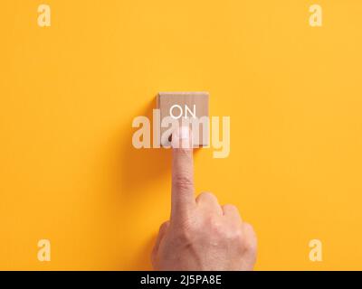 Male hand presses on a wooden cube with the word on. Power on push button business startup activation concept. Stock Photo