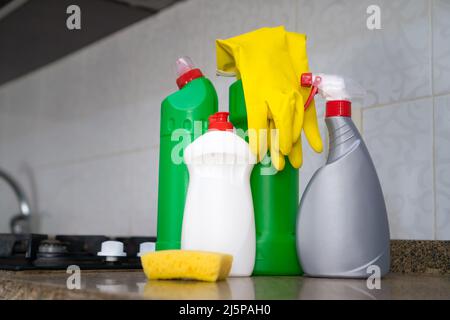 Close-up of cleaning products, yellow rubber gloves, a sponge on the kitchen table near the gas stove. Concept of cleaning, household chores Stock Photo