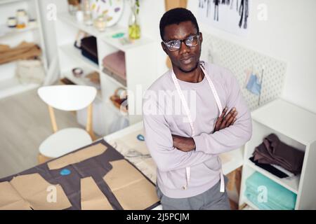 Young confident atelier owner standing at table with fabric and cardboard sewing pattern Stock Photo